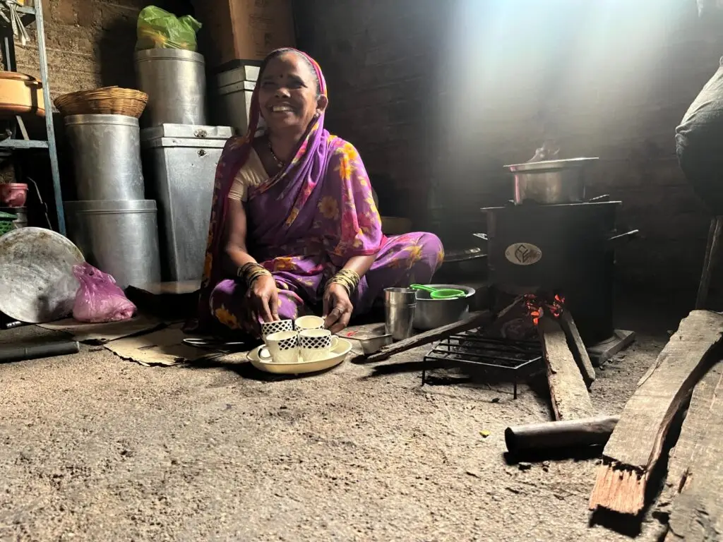 Smiling rural woman using eco-friendly cookstove in traditional Indian kitchen – promoting clean cooking solutions