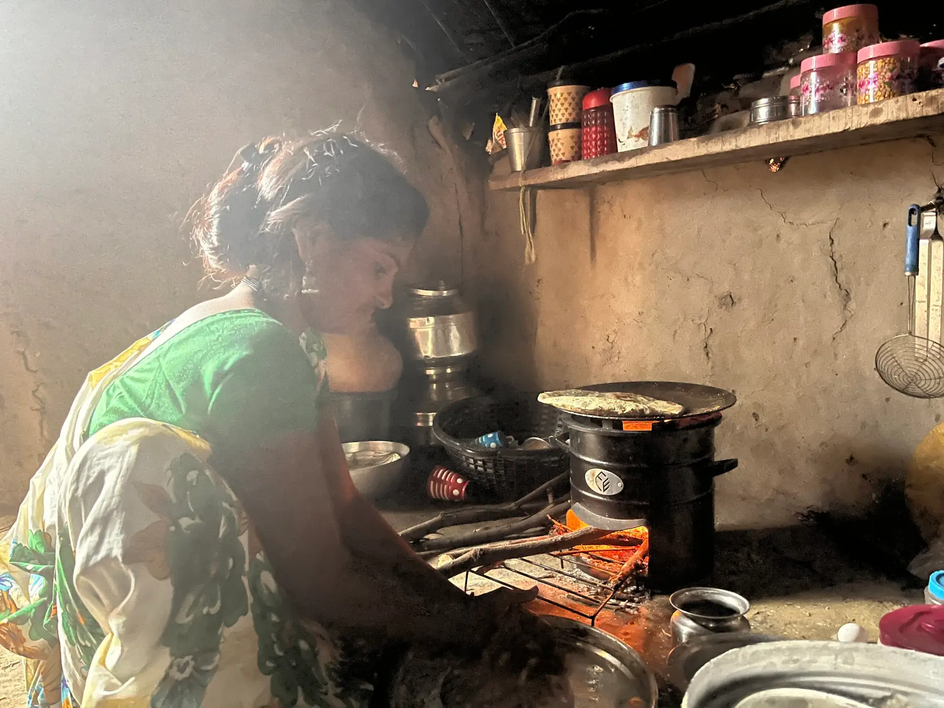 Woman smiling while cooking on an Earthfit clean cookstove in a kitchen, demonstrating eco-friendly and efficient cooking.